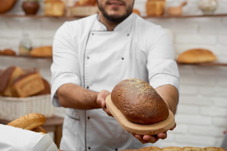 A man is holding a loaf of bread in front of a Kosher bakery.
 Richmond Kosher Bakery