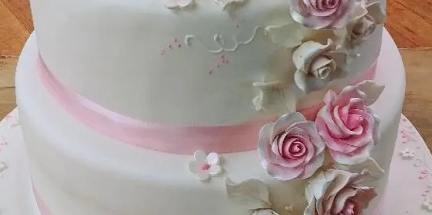 A kosher white cake adorned with pink roses on top. Richmond Kosher Bakery